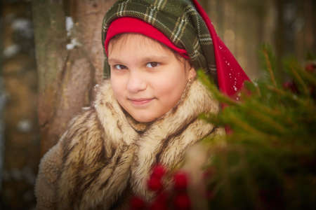Portrait of a nice cute teenager girl in old peasant clothes with hot fur coat and shawl in cold winter forest with fir trees, pines and snow on winter dayの写真素材