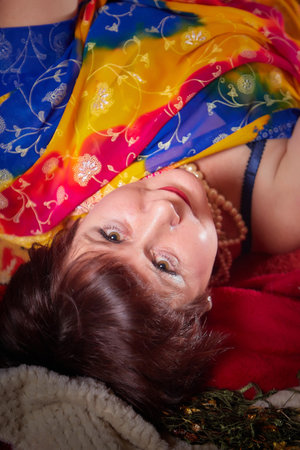 A beautiful European girl with short hair looking like an Arab woman in a red room in a harem. Photo shoot of an oriental style odalisque. A model poses in a sariの写真素材