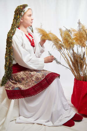 Beautiful smiling girl in stylized slavic red and white national costume on white background. Funny woman and model posing in studio with ears of cornの写真素材