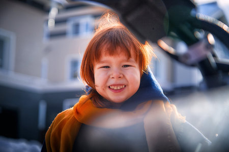 Stylish happy kid girl 2-3 year old with redhair wear blue coat and yellow scarf walk in city street in winter, autumn or spring season with snowの写真素材