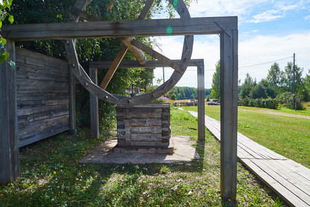 An old wooden wall with a wheel and a bucket on a chain against the backdrop of old villageの写真素材