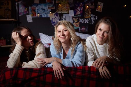 Kirov, Russia - January 04, 2022: Beautiful happy young women girlfriends with hair and makeup have fun on the bed in dark room decorated for Christmas and New Yearのeditorial素材