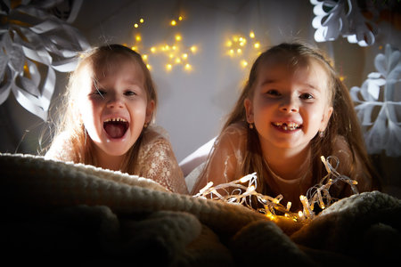 Portrait of a little pretty girls with long beautiful hair in red dress in the room decorated for Christmas with garland lights and dark background. Christmas and New Year holidayの写真素材