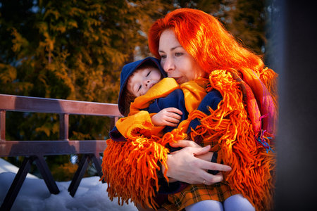 Mother with red hair and a fluffy orange jacket and a little daughter walking in winter, autumn or spring in the village and snow. The concept of love and friendship of mom and girlの写真素材