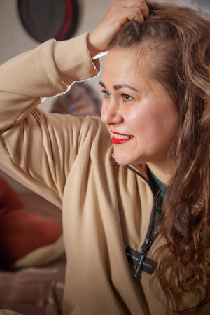 Kirov, Russia - January 03, 2022: Charming adult overweight lady with dark long hair and positive cute smile at home, smiling happily in living room in Christmas winterのeditorial素材