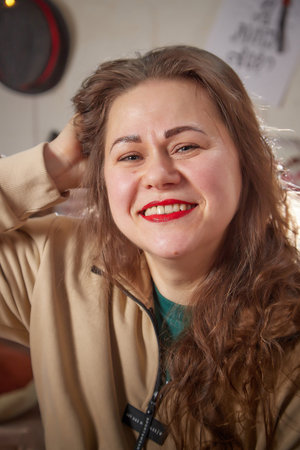 Kirov, Russia - January 03, 2022: Charming adult overweight lady with dark long hair and positive cute smile at home, smiling happily in living room in Christmas winterのeditorial素材