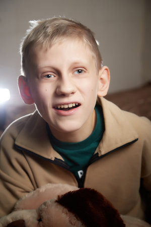 Kirov, Russia - January 03, 2022: Portrait of a handsome disabled boy with autism and cerebral palsy in warm sweater in the room decorated for Christmas with nice lights. Kid's winter fashionのeditorial素材