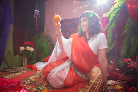 Beautiful European girl looking like Arab woman in red room with rich fabrics and carpets in sultan harem. Photo shoot of an oriental style odalisque. A model poses in sari as an indian woman in indiaの写真素材