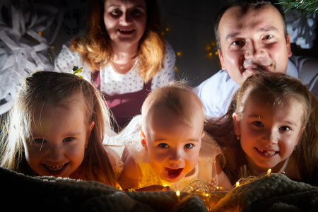 Christmas portrait of big family with father, mother and three sisters in home holiday living room decorated for holiday with light of garlandの写真素材