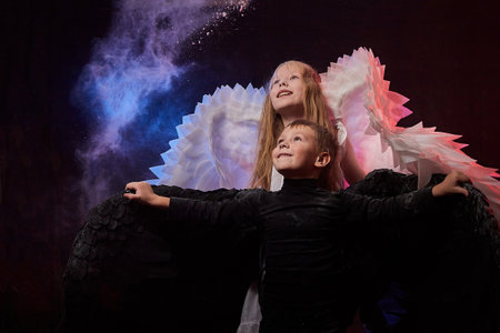 Boy in black clothes and girl in white dress with angel or demon wings. Concept of struggle of good...