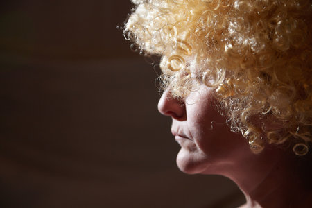 Portrait of woman in white blonde wig with dandelions. Female model posing in studio for dark picture with lightの写真素材