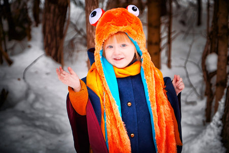 Portrait of Little girl in blue coat, yellow scarf and a red hat with frog eyes in winter in nature in countryside with snow and forestの写真素材