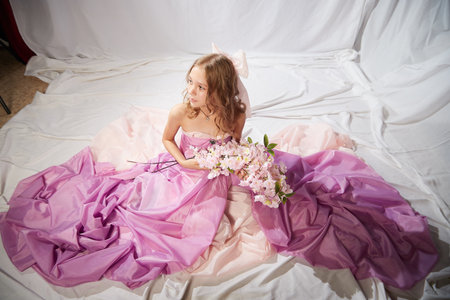 Portrait of cute kid girl posing in pink beautiful dress on a white background. Model in studio looking as gentle magic princess from fairy taly having photo shoot on white backgroundの写真素材