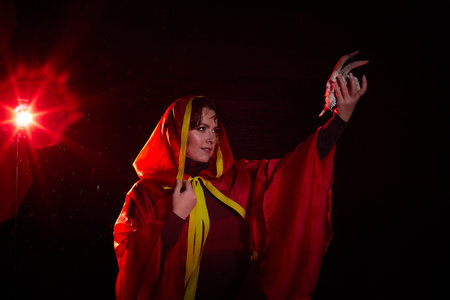 Witch woman in red cloak with skull on black background and light in night. Female warrior in Darkの写真素材