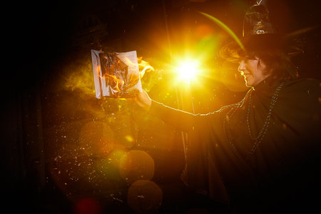 Halloween Witch girl with fier on magic Book of spells portrait. Beautiful young woman in hat...