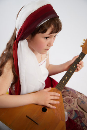 Portrait of Little girl in a stylized Tatar national costume with a musical instrument balalaika on a white background in the studio. Photo shoot of funny young teenager who is not professional modelの写真素材
