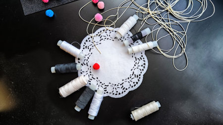 White and black spools of thread with decorative napkin and colored soft fluffy balls on a black...