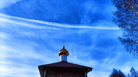 The dome of the Orthodox church with a cross, bare tree branches and blue sky with white clouds on a background in spring dayの写真素材
