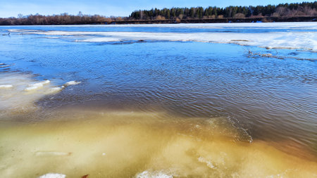 Spring landscape with water, ice, snow on river, trees without leaves and blue sky in the background in sunny day. Ice drift and flood on river with sunの写真素材