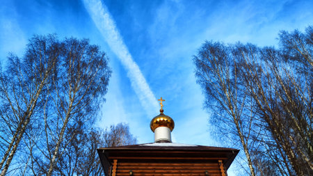 The dome of the Orthodox church with a cross, bare tree branches and blue sky with white clouds on a background in spring dayの写真素材