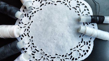 White and black spools of thread with decorative napkin on black background. Black card with...