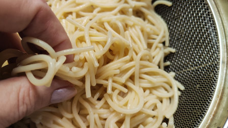 Yellow white thin strands of noodles in the metal bowl. Raw and uncooked. Cooking noodles in boiling water and rinsing vermicelli or spaghetti with water by woman handの写真素材