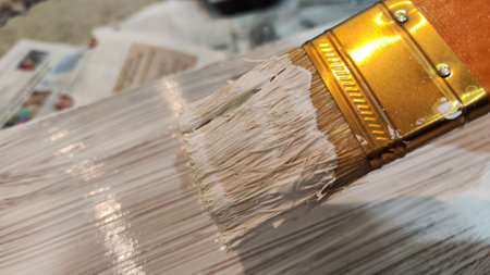 Brush with white paint is on boards. Painting of new wood board or furniture and old newspaper on...