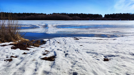 Spring landscape with water, ice, snow on river, trees without leaves and blue sky in the background in sunny day. Ice drift and flood on river with sunの写真素材