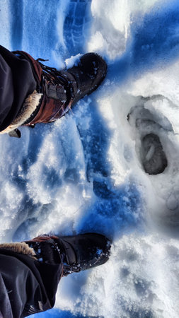 Feet of Hunter or fisherman in big warm boots on a winter day on snow. top view. A fisherman on the ice of river, lake, reservoir on a spring day with melting ice. Dangerous fishingの写真素材
