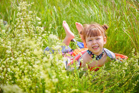 Portrait of a little girl with Asian eyes in a meadow or field with grass and flowers on a sunny summer dayの写真素材