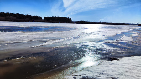 Spring landscape with water, ice, snow on river, trees without leaves and blue sky in the background in sunny day. Ice drift and flood on river with sunの写真素材