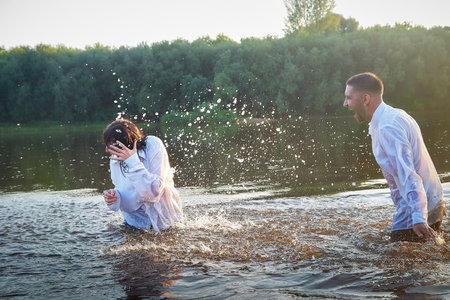 A beautiful adult couple has fun in nature in the water in a river or lake in the summer evening at...