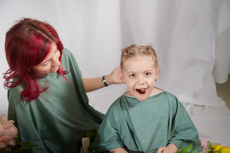 Amazing pretty mother and daughter having fun with flowers in 8 March or in Mothers day. Red haired mom and small little blonde girl having lovely free time on white backgroundの写真素材