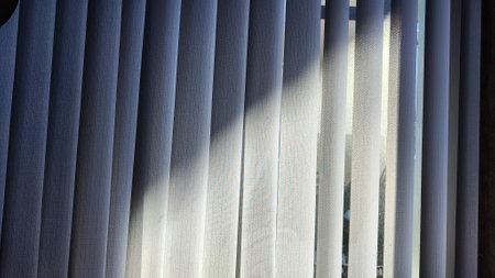 Vertical fabric white blinds on the window with light and shadow from sun. background and texture....