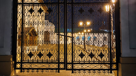 Iron grille in the entrance with low yellow light and big yard on background in dark night time....