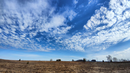 Beautiful blue sky with white clouds on a sunny autumn or spring day over field with dry grass. Natural background and copy space. Landscape in early spring or autumnの写真素材