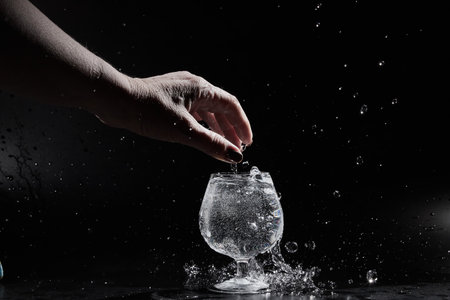 Fingers of hand of a woman touching water or mineral water in a wine glass on black backgroundの写真素材
