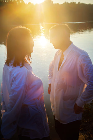 Happy Couple relaxin, having fun and hugs on nature near water of river or lake in summer sunny evening during sunset. Family or lovers have date and rest outdoors. Concept of love and friendshipの写真素材