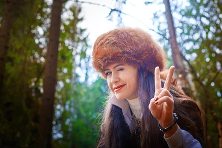 Girl in a leather jacket, a big red fox fur hat in the forest in autumn. A female model poses as a...