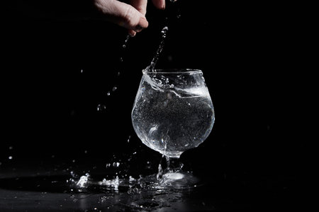 Fingers of hand of a woman touching water or mineral water in a wine glass on black backgroundの写真素材