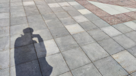Gray tiles on sidewalk in the city outdoors and the shadow of the traveler photographer. Background...