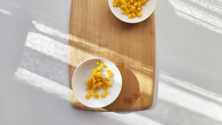 Lot of pieces of canned yellow corn on plate which is on wooden bamboo cutting board on white background. Concept of cooking and delicious food healthyの写真素材