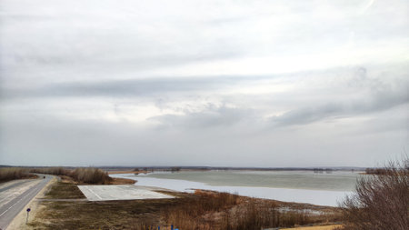 Landscape with the water of lake, river, bay or reservoir with gray water, gloomy sky and clouds and...