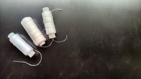 White spools of thread on a black background. Black card with texture, frame and sewing threads....