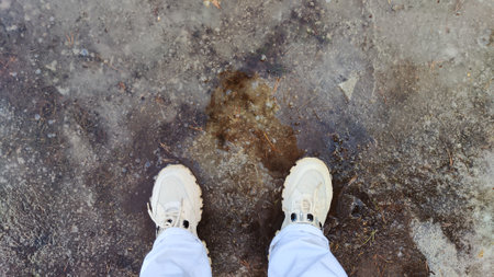 Feet in white sneakers and jeans on ice, road and asphalt. Clothes for a walk in spring. Spring weather and travel concept. Background, texture or abstract frameの写真素材