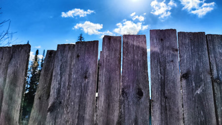 Old wooden planks in fence and blue sky with white clouds. background and texture. Abstract frame and copy space. Ancient Wooden rustic rural fence and nature landscapeの写真素材