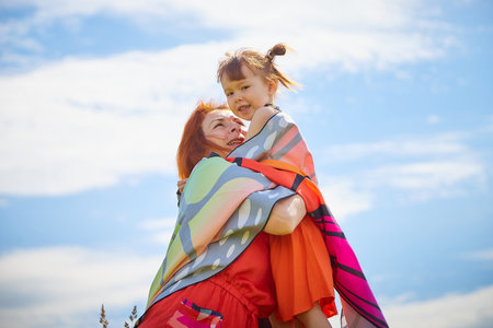 Happy female family with red haired mother and daughter with bright butterfly wings having fun on green and yellow meadow full of grass and flowers in sunny summer day. concept family loveの写真素材