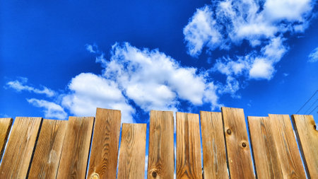 Old wooden planks in fence and blue sky with white clouds. background and texture. Abstract frame and copy space. Ancient Wooden rustic rural fence and nature landscapeの写真素材