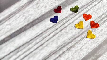 Multicolored hearts made of rough velvet paper on white surface with stripes of shadow and light...