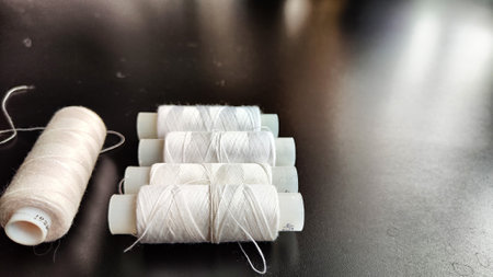 White spools of thread on a black background. Black card with texture, frame and sewing threads. Partial focusの写真素材